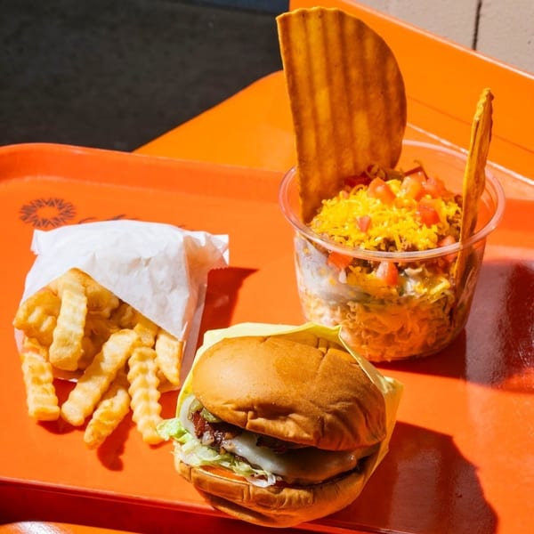 Naugles Tacos combo meal with a burger, crinkle-cut fries, and a taco salad on an orange tray.