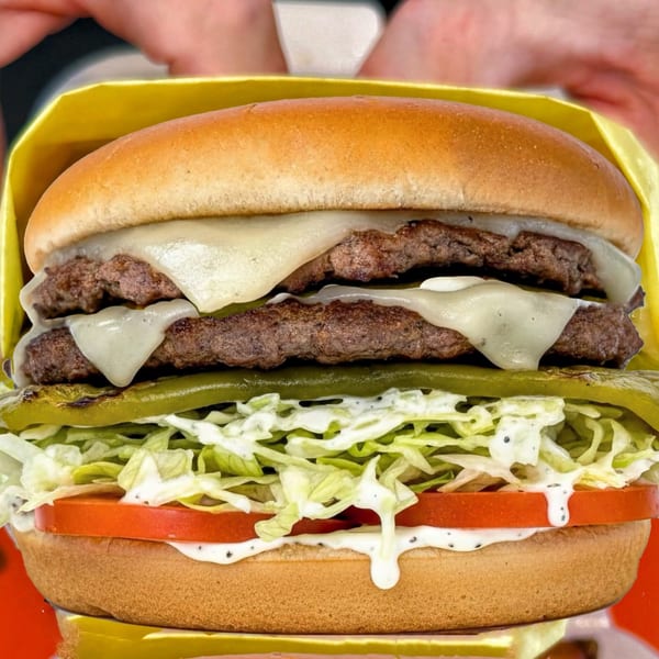 Close-up of a double cheeseburger with melted cheese, lettuce, tomato, pickles, and sauce on a bun.