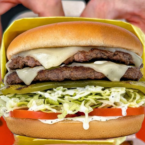 A double cheeseburger with melted cheese, grilled green chiles, shredded lettuce, tomato, and sauce.