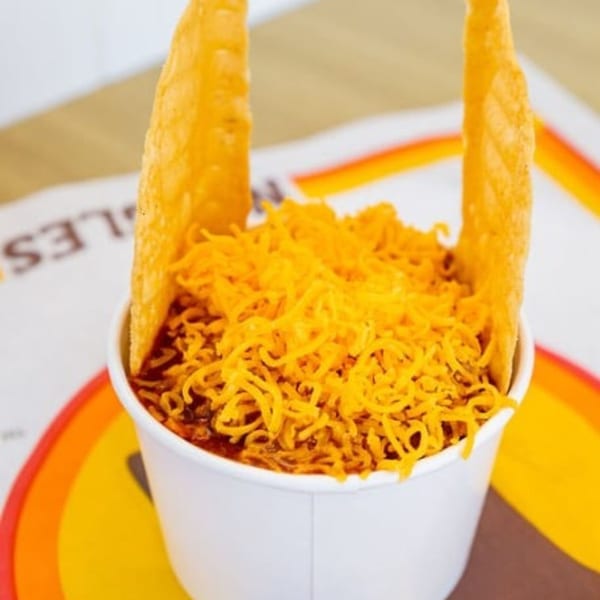 Naugles Tacos' chili cheese burrito in a cup, topped with shredded cheese and two tortilla chips.