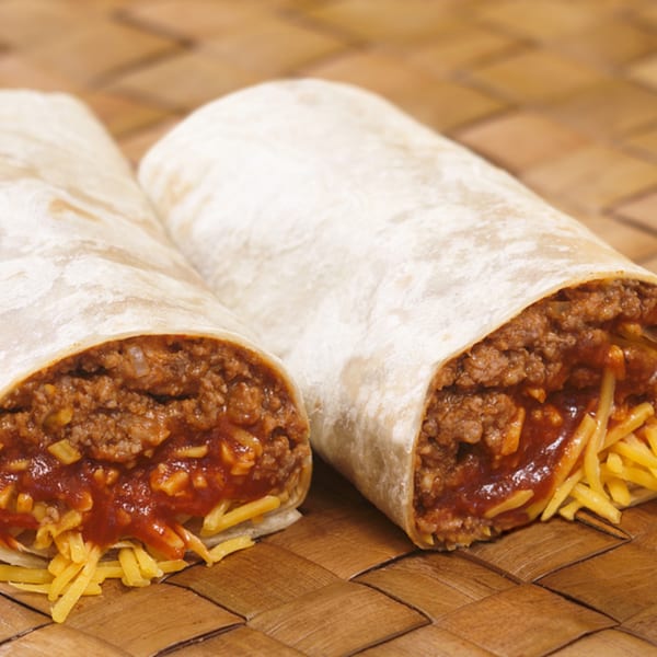 Two burritos, cut open to reveal ground beef, red sauce, and shredded cheese, on a woven mat.