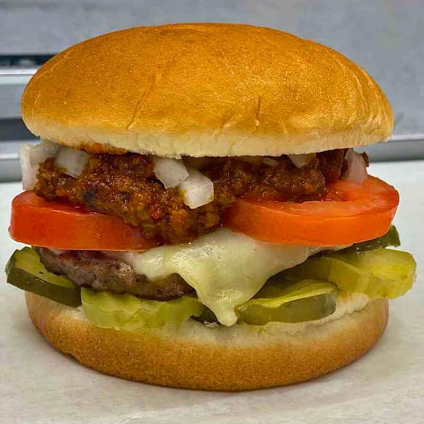 A chili cheeseburger with diced onions, tomato, melted cheese, and pickles on a bun.