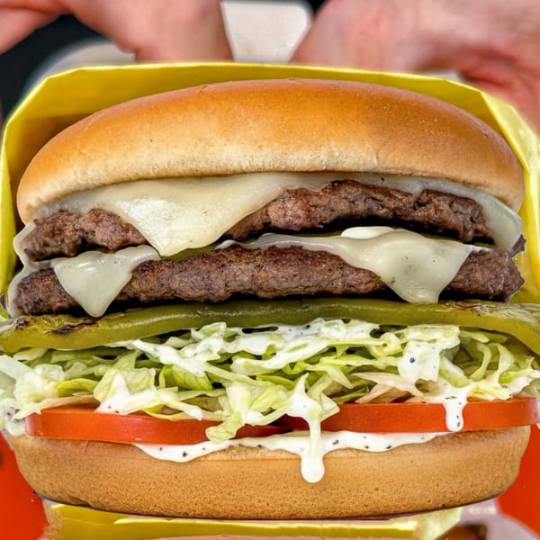 A double cheeseburger with melted cheese, grilled peppers, shredded lettuce, tomato, and sauce.