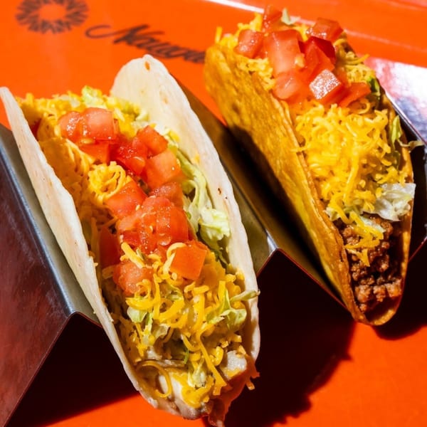Two Naugles Tacos, one soft and one hard shell, filled with meat, cheese, lettuce, and tomatoes.
