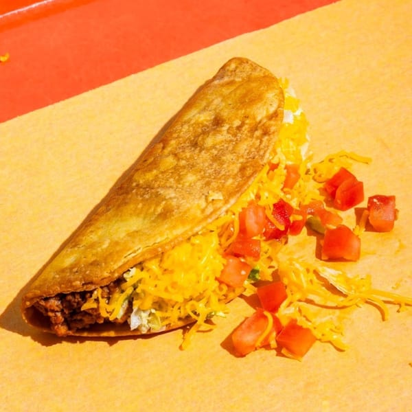 Naugles Tacos' crispy taco filled with meat, cheese, lettuce, and diced tomatoes on a yellow surface.