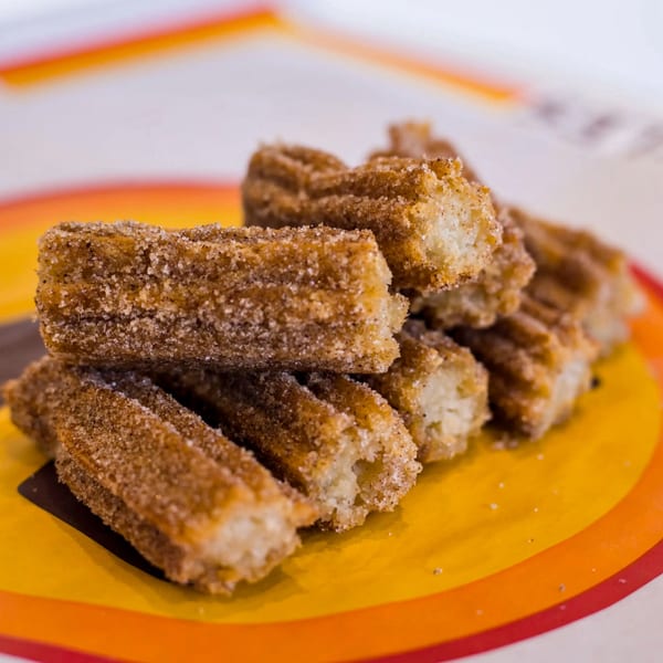 A pile of golden-brown churros coated in cinnamon sugar, on a colorful plate.