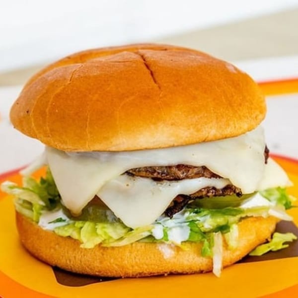 Naugles Tacos' burger with melted cheese, shredded lettuce, and white sauce on a bun.
